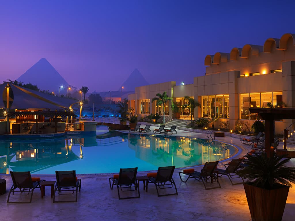 Luxury Egyptian resort at twilight with pool and the Great Pyramids of Giza in the distance